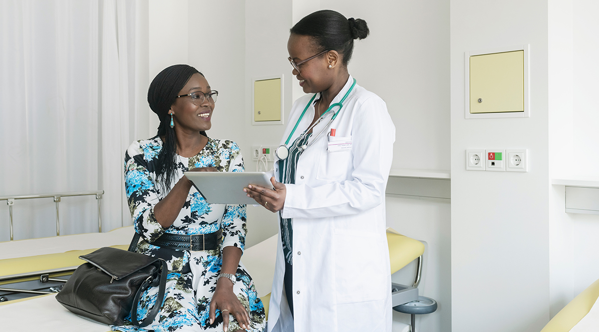 A physician reviewing a note on a tablet with a patient